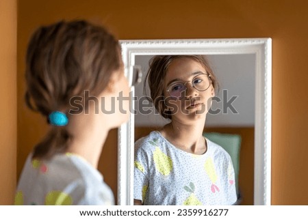 A teenage girl looks at herself in the mirror in the morning. Royalty-Free Stock Photo #2359916277