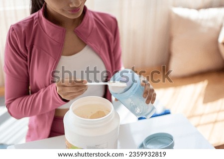Close-up image of a healthy and fit Asian woman in sportswear making her protein shake after a workout at home. Drink supplements, high-nutrition drinks, diet, and muscle-building Royalty-Free Stock Photo #2359932819