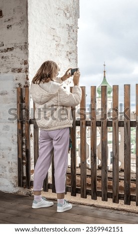 A female tourist on the observation deck takes pictures of landmarks on her smartphone.