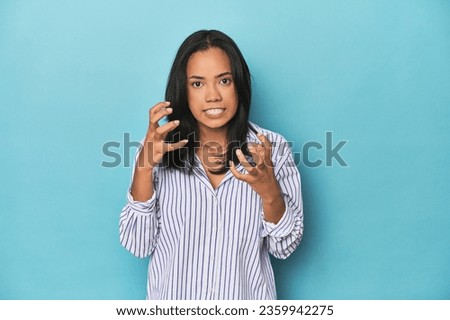 Filipina young woman on blue studio upset screaming with tense hands.