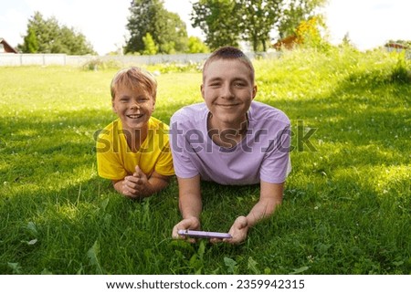 Two happy broters lying on green grass in meadow with cellphone. children looking at mobile phone screen outside