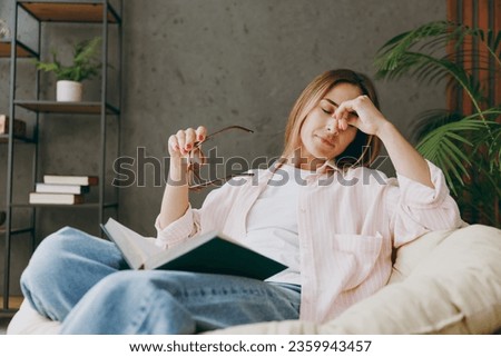 Tired exhausted sad young woman wear casual clothes take off glasses sits in armchair read book stay at home hotel flat rest relax spend free spare time in living room indoor. Lifestyle lounge concept Royalty-Free Stock Photo #2359943457