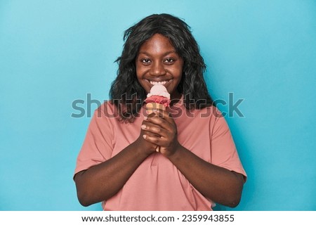 Young curvy woman enjoying ice-cream on a blue backdrop