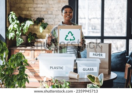 Young plus size African American woman holding symbol of recycling, environment protect. Doing home garbage sorting , care about planet, ecology. Containers for recyclable waste: plastic, glass, paper