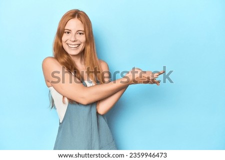 Redhead young woman on blue background holding a copy space on a palm.
