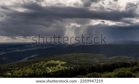 Panoramic view of sun rays shining through rainclouds showing thefalling rain in Northern Israel looking towards the Mediterranean Sea from Muhraqa viewpoint.
 Royalty-Free Stock Photo #2359947219