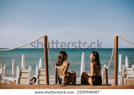 Two smiling young women in bikini sitting and enjoying vacation on the beach