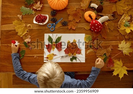 Child, applying leaves using glue, scissors, and paint, while doing arts and crafts at home or at school