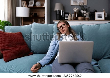 Young business woman fell asleep on sofa while working on laptop. Overworked tired woman tired of working on computer from home office sleeping with laptop on lap. Royalty-Free Stock Photo #2359962569