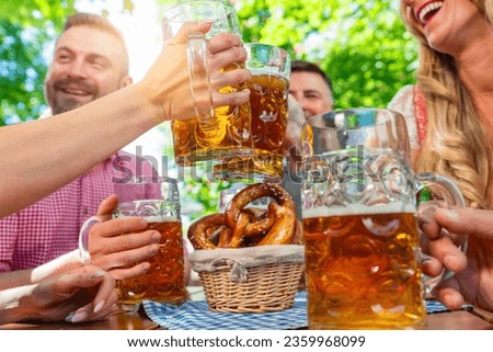 friends in Tracht, Dirndl and Lederhosen having fun sitting on table drinking beer and eating pretzels in Beer garden or oktoberfest in Bavaria, Germany Royalty-Free Stock Photo #2359968099