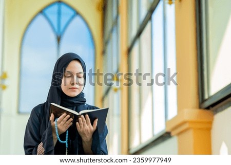 The image of an Asian Muslim woman in the Islamic religion in hijab in black  color. reading the Quran and having a happy Staying in a beautiful mosque, Arabic word translation: The Holy Al Quran.