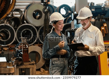 Factory engineer manager with assistant using laptop to conduct inspection of steel industrial machine, exemplifying leadership as machinery engineering inspection supervisor in metalwork manufacture. Royalty-Free Stock Photo #2359979277