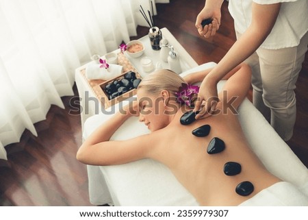 Hot stone massage at spa salon in luxury resort with day light serenity ambient, blissful woman customer enjoying spa basalt stone massage glide over body with soothing warmth. Quiescent Royalty-Free Stock Photo #2359979307