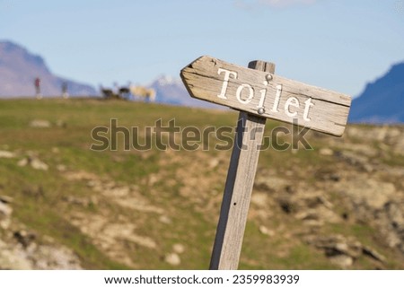 Outdoor toilet sign in grassland and mountains. Rustic wooden sign with the word Toilet