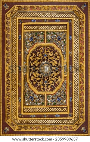 A delicately carved wooden picture frame, painted in gold and a deep red background, decorated with cut-and-pasted glass, gemstones, and pearls.