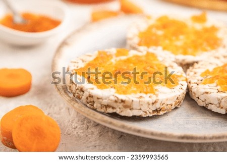 Carrot jam with puffed rice cakes on gray concrete background. Side view, close up, selective focus.