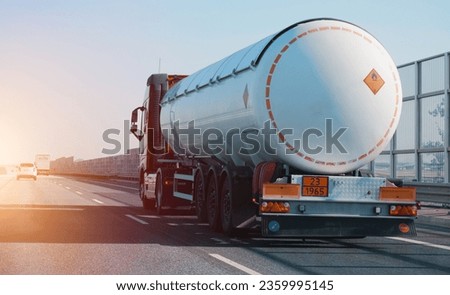 Petrol cargo truck driving on highway hauling oil products. Fuel delivery transportation and logistics concept on a sunny summer evening. Compressed gas carrier truck rear view on a highway. Royalty-Free Stock Photo #2359995145