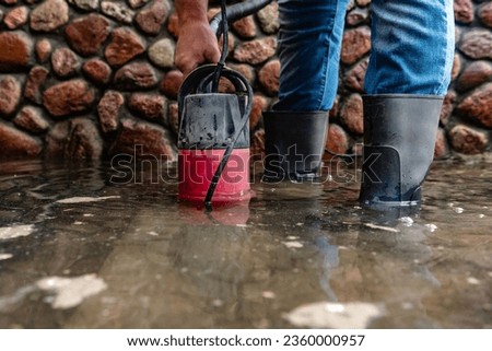 A man pumps out water at the entrance to the garage using a submersible pump. Royalty-Free Stock Photo #2360000957