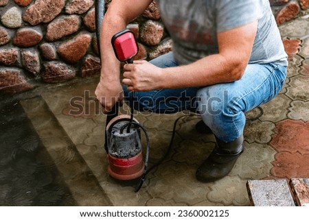 A man pumps out water at the entrance to the garage using a submersible pump. Royalty-Free Stock Photo #2360002125