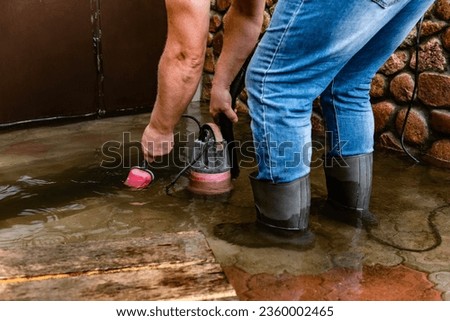 A man pumps out water at the entrance to the garage using a submersible pump. Royalty-Free Stock Photo #2360002465