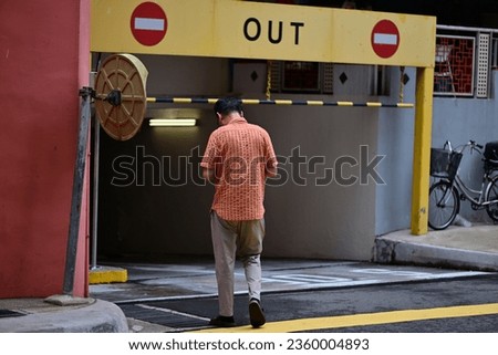 A man walks the wrong way into a parking garage in Singapore. Two stop signs on yellow background.