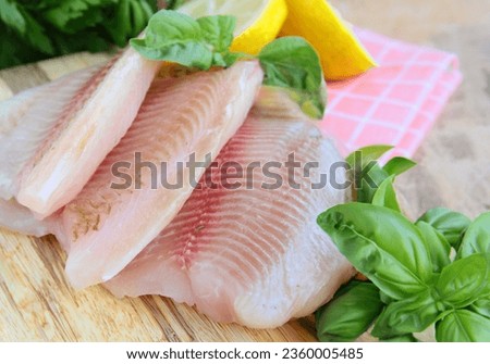 fresh raw tilapia fish fillet on wooden board Royalty-Free Stock Photo #2360005485