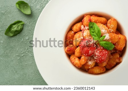 Potato gnocchi. Traditional homemade potato gnocchi with tomato sauce, basil and parmesan cheese on kitchen table on light green kitchen table background. Traditional Italian food. Top view. Royalty-Free Stock Photo #2360012143