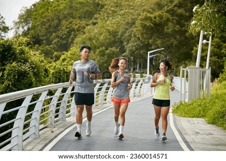 three young asian women female joggers exercising outdoors together in city park Royalty-Free Stock Photo #2360014571