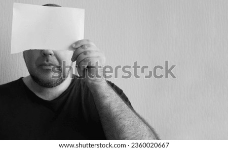 Portrait of a man holding a piece of white paper behind eyes. isolated on white background. mock up sheet. Male holding near own head, face. Unrecognizable person. businessman holding a card. mockup.