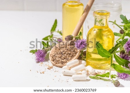 Milk Thistle supplies, powder and oil. Silybum marianum, natural organic wild flower superfood product - whole and grain seeds, pills, oil with fresh thistle flowers Royalty-Free Stock Photo #2360023769