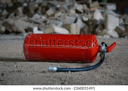 A vibrant red fire extinguisher set against a background of grey and white stones