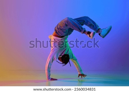Flexible young man, contemp dancer performing breakdance, hip-hop against gradient multicolored studio background in neon light. Concept of street style dance, fashion, youth, hobby, dynamics, ad Royalty-Free Stock Photo #2360034831