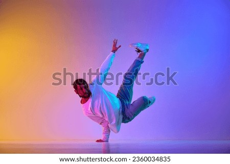 Dance show. Young guy dancing contemp, breakdance and hip-hop against gradient multicolored studio background in neon light. Concept of street style dance, fashion, youth, hobby, dynamics, ad