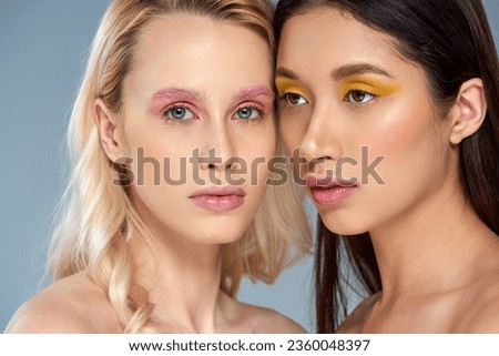 diverse beauty concept, interracial women with bold eye makeup posing on blue background, feminine