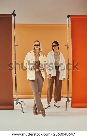 interracial models in sunglasses and autumn outerwear posing in studio, fall colors, duo backdrop