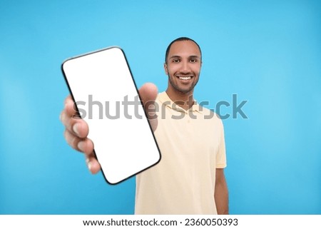 Young man showing smartphone in hand on light blue background Royalty-Free Stock Photo #2360050393