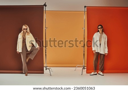 autumn fashion, stylish multicultural models in sunglasses and outerwear posing on colorful backdrop