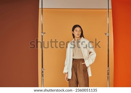 pretty asian woman in autumn outfit posing with hand in pocket, leather pants and outerwear Royalty-Free Stock Photo #2360051135