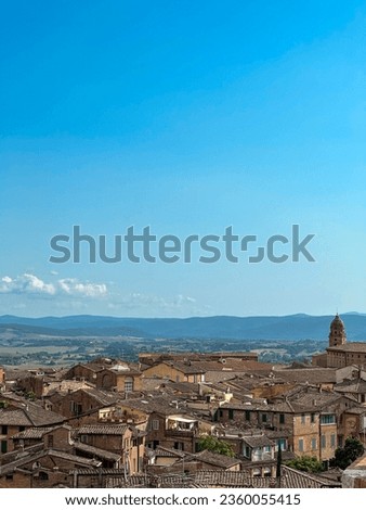 Panoramic shot capturing the breathtaking landscape of Siena from an elevated viewpoint. The city unfolds, showcasing its terracotta roofs, historic landmarks, and the surrounding Tuscan countryside.