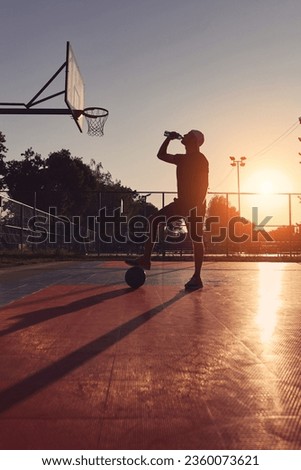 Man drinking water on with public basketball court.
