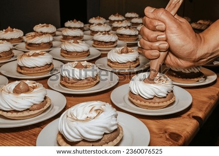 A picture of a hand using a pipe bag to fill the dessert pieces on a table. Chef in action, tasty food. One person, horizontal image.