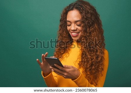 Beautiful young woman texting on cellphone, smiling, green studio background Royalty-Free Stock Photo #2360078065