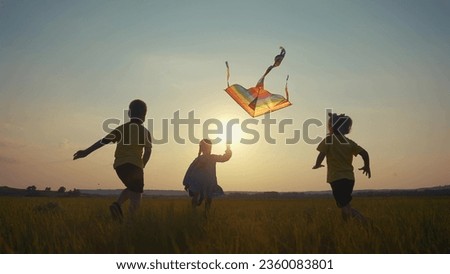 children run with a kite in the park. happy family kid dream concept. a group of children run in the park in nature at sunset playing with kite. kids silhouette play together in park with sun kite