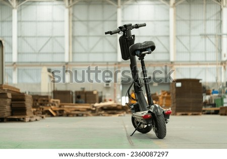 An electric scooter is parked in a large factory warehouse. It is necessary for the convenience of the factory manager. Royalty-Free Stock Photo #2360087297