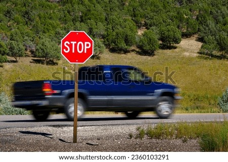 Bright red stop sign on road with blurry blurred moving car or truck speeding past 