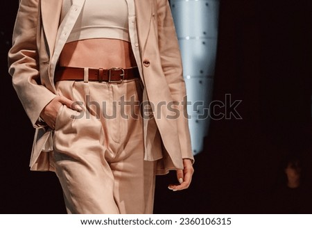 Figure of fashion model woman wearing beige classy casual costume, pants and jacket on black background. Fashion stylish shot. Street style clothes concept