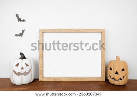 Halloween mock up. Wooden frame on a wood shelf with jack o lantern decor. Landscape frame against a white wall. Copy space.