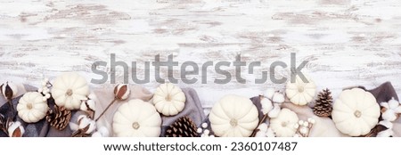 Cozy autumn bottom border with blanket, white pumpkins natural decor. Top down view over a white wood banner background. Black, white and brown theme.
