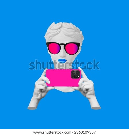 Antique statue's head in sunglasses holding pop pink mobile phone with photo camera in hands taking picture on bright blue color background. 3d trendy creative collage. Contemporary art. Modern design