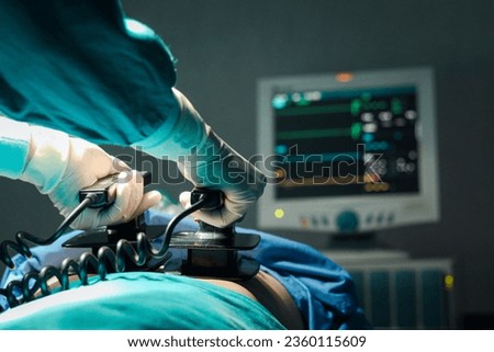 Surgeon doctor hand hold defibrillator to pump chest heart patient to save life sick people in operating room at hospital, surgical team using equipment to do surgery. healthcare and medical concept. Royalty-Free Stock Photo #2360115609